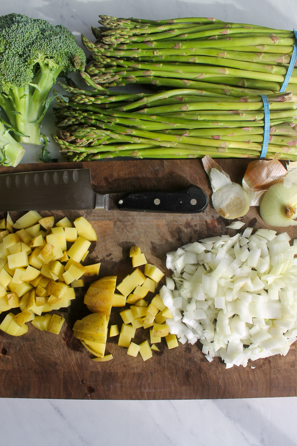 A cutting board with chopped potato and onion and asparagus and broccoli next to it.