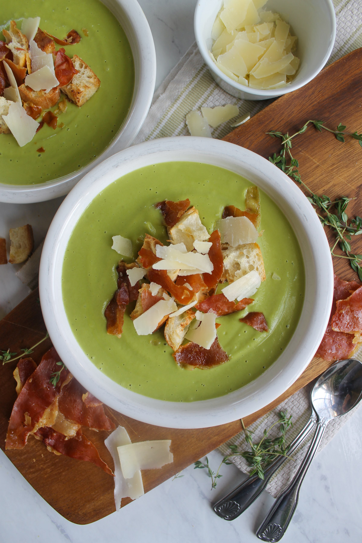 A bowl of green blended Asparagus Broccoli Soup with croutons, crispy prosciutto and Parmesan cheese toppings.