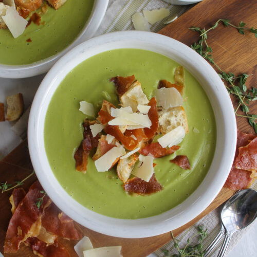 A white bowl of Broccoli Asparagus Soup topped with crispy prosciutto and croutons.