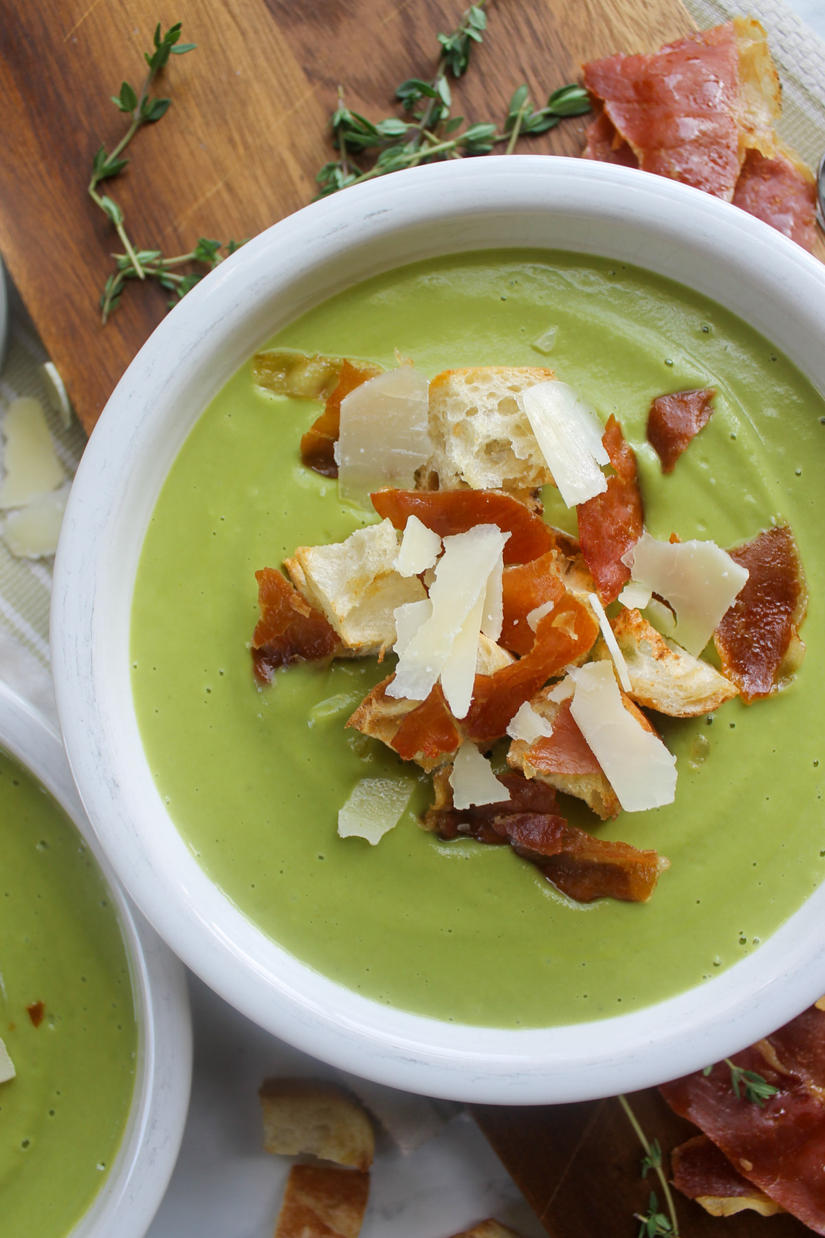A bowl of green soup on a cutting board with toppings and fresh thyme.