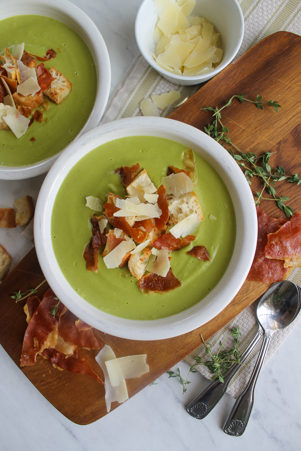 A bowl of green blended Asparagus Broccoli Soup with croutons, crispy prosciutto and Parmesan cheese toppings.