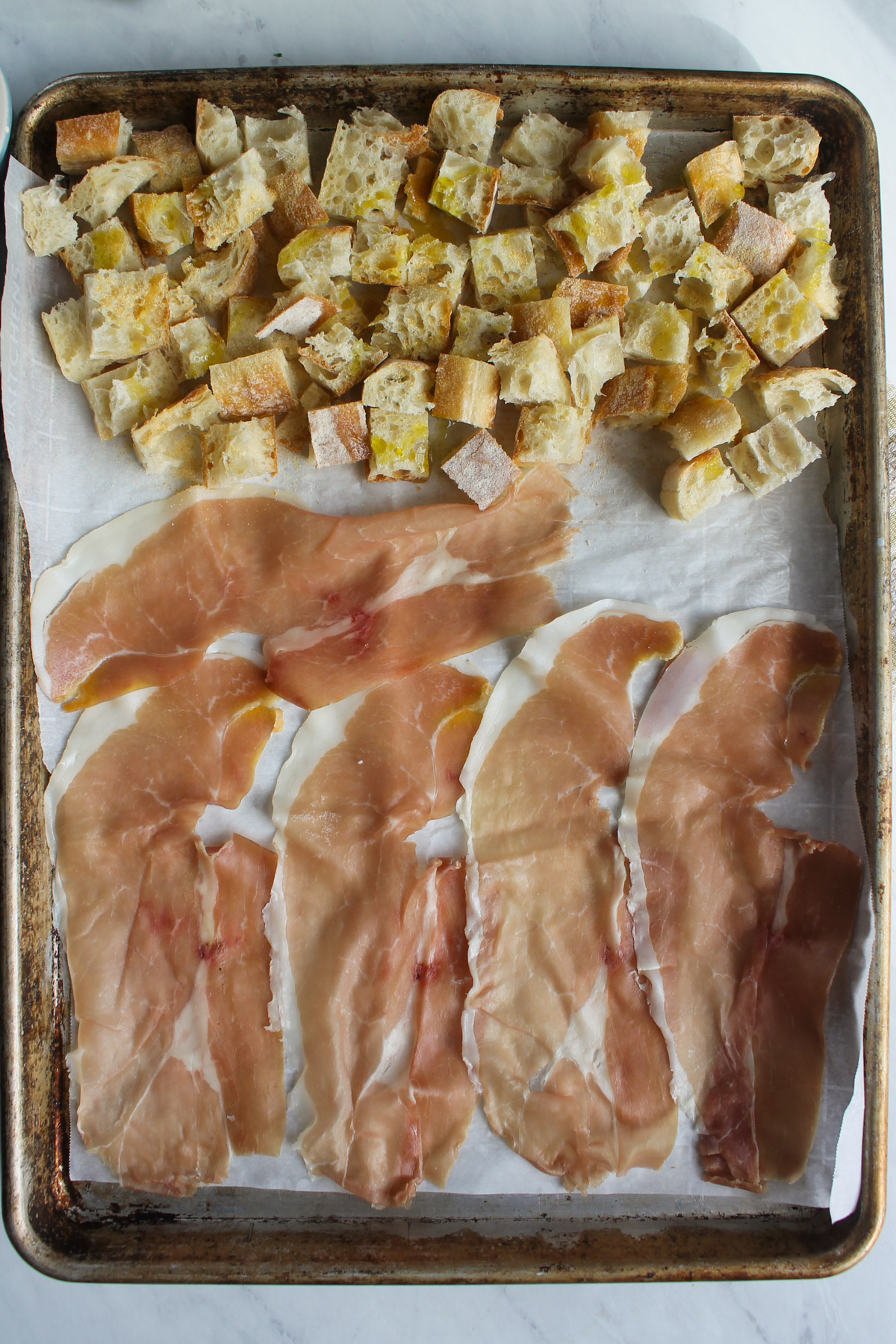 Raw croutons and prosciutto on a sheet pan ready to bake.