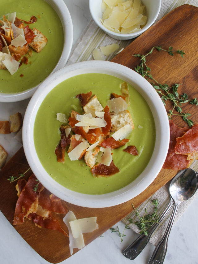 A bowl of green blended Asparagus Broccoli Soup with croutons, crispy prosciutto and Parmesan cheese toppings.