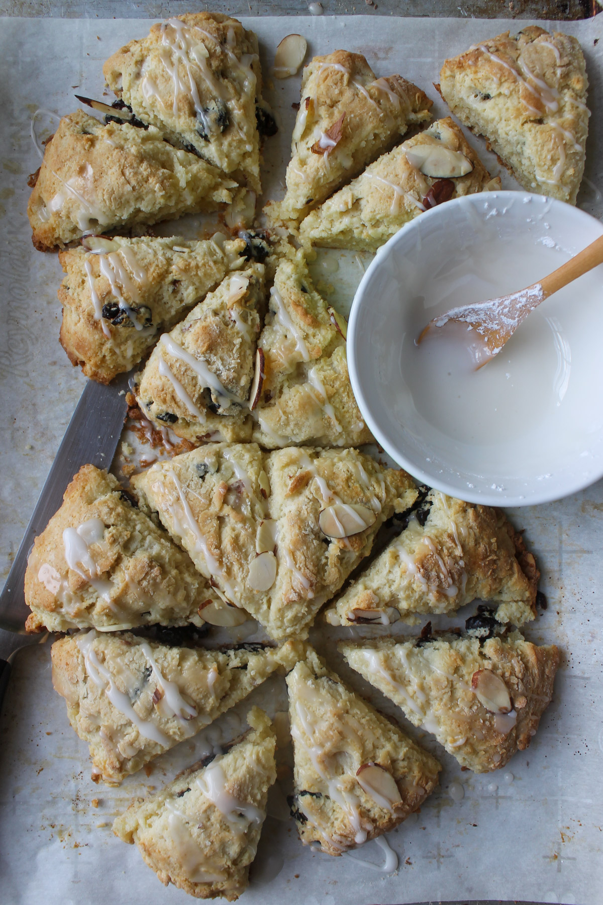 Two round disks of scones cut into wedges on parchment paper with a bowl of glaze.