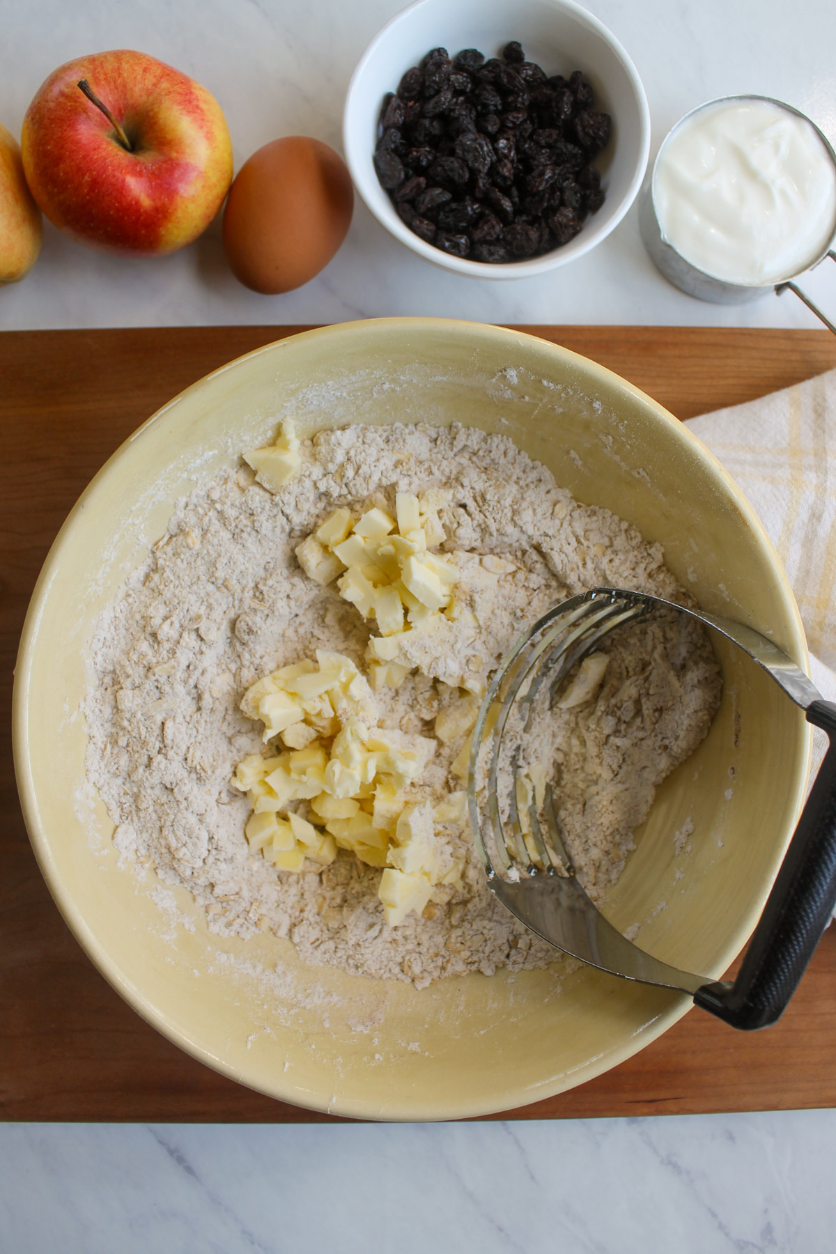 Cutting the butter into the flour mixture with a pastry cutter in a yellow bowl.