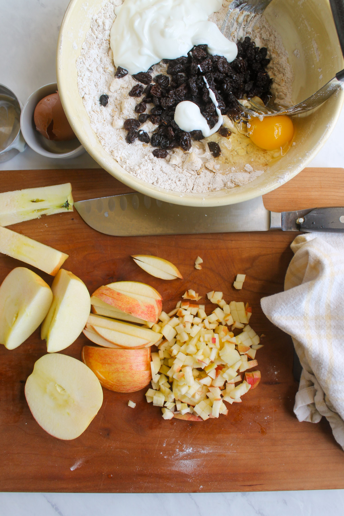 Apples diced small on a cutting board next to a bowl of scone batter.