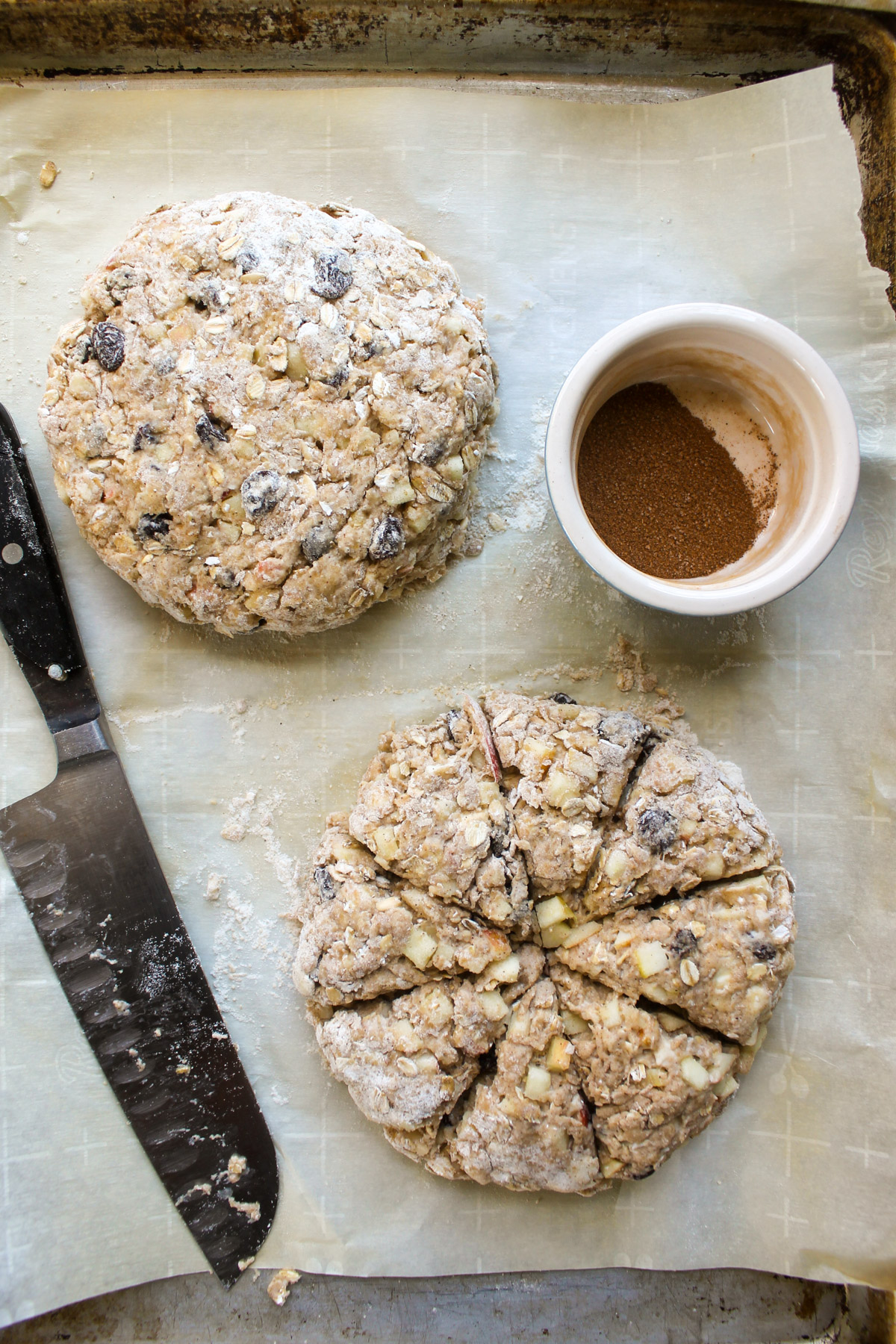 Two round disks of scone dough on a sheet pan with parchment paper cut into wedges.