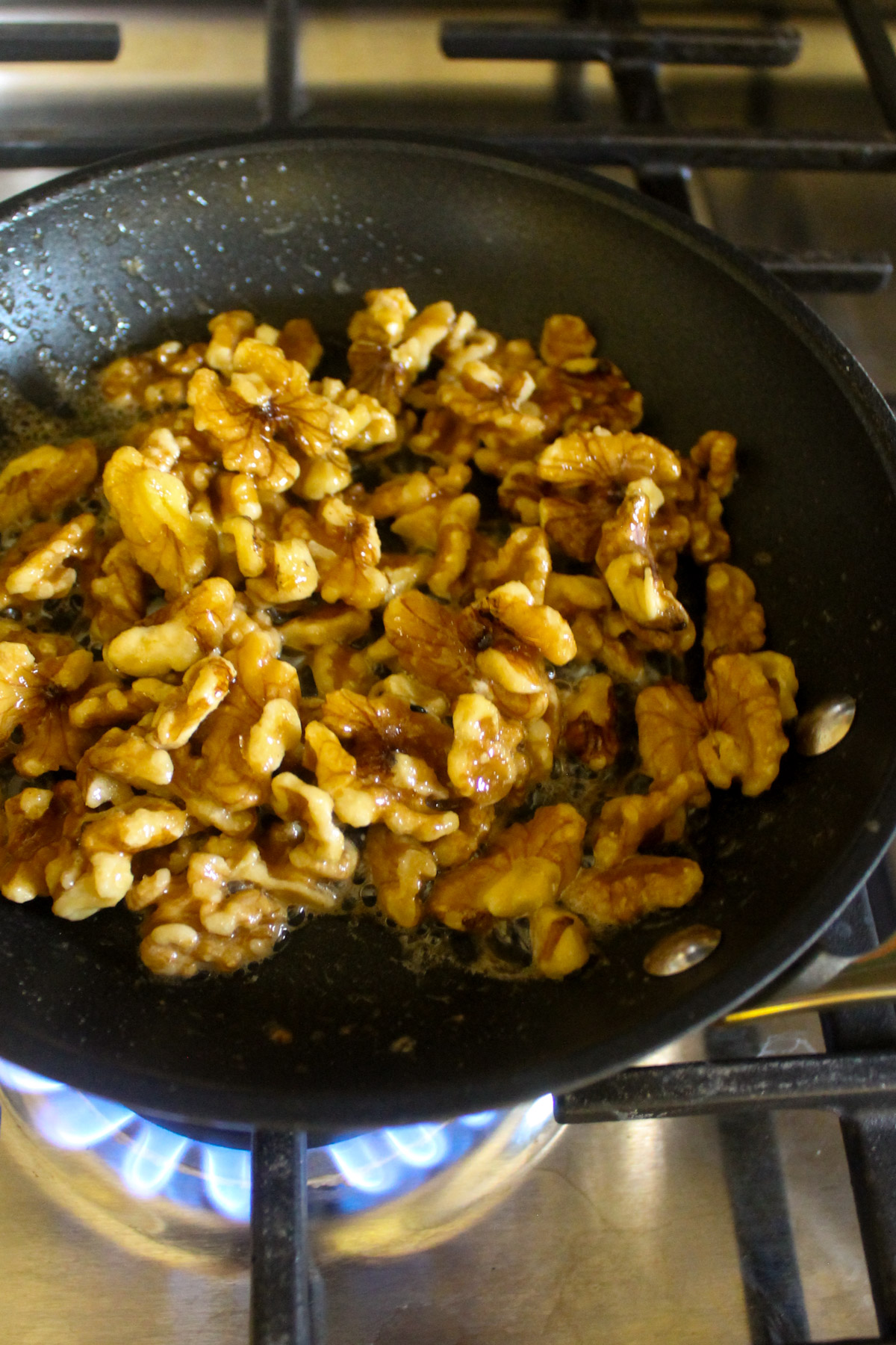 Toasting candied walnuts in a skillet with butter and brown sugar.