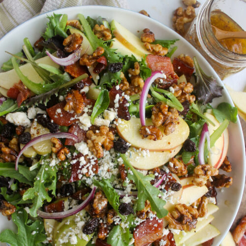 A platter of Blue Cheese Apple Walnut Salad with a jar of dressing.