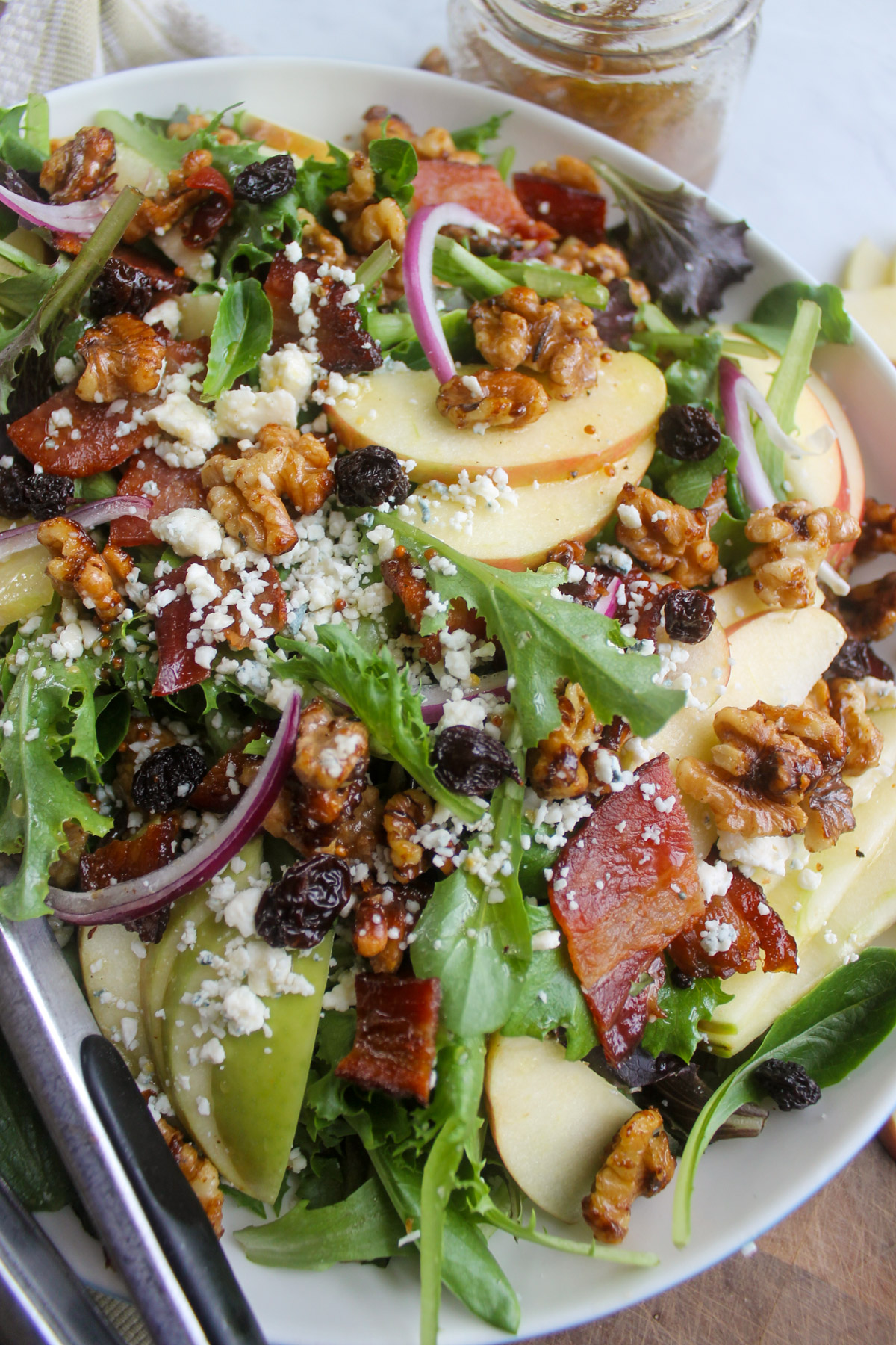 A salad with slices of apple, raisins, onions, blue cheese and nuts.