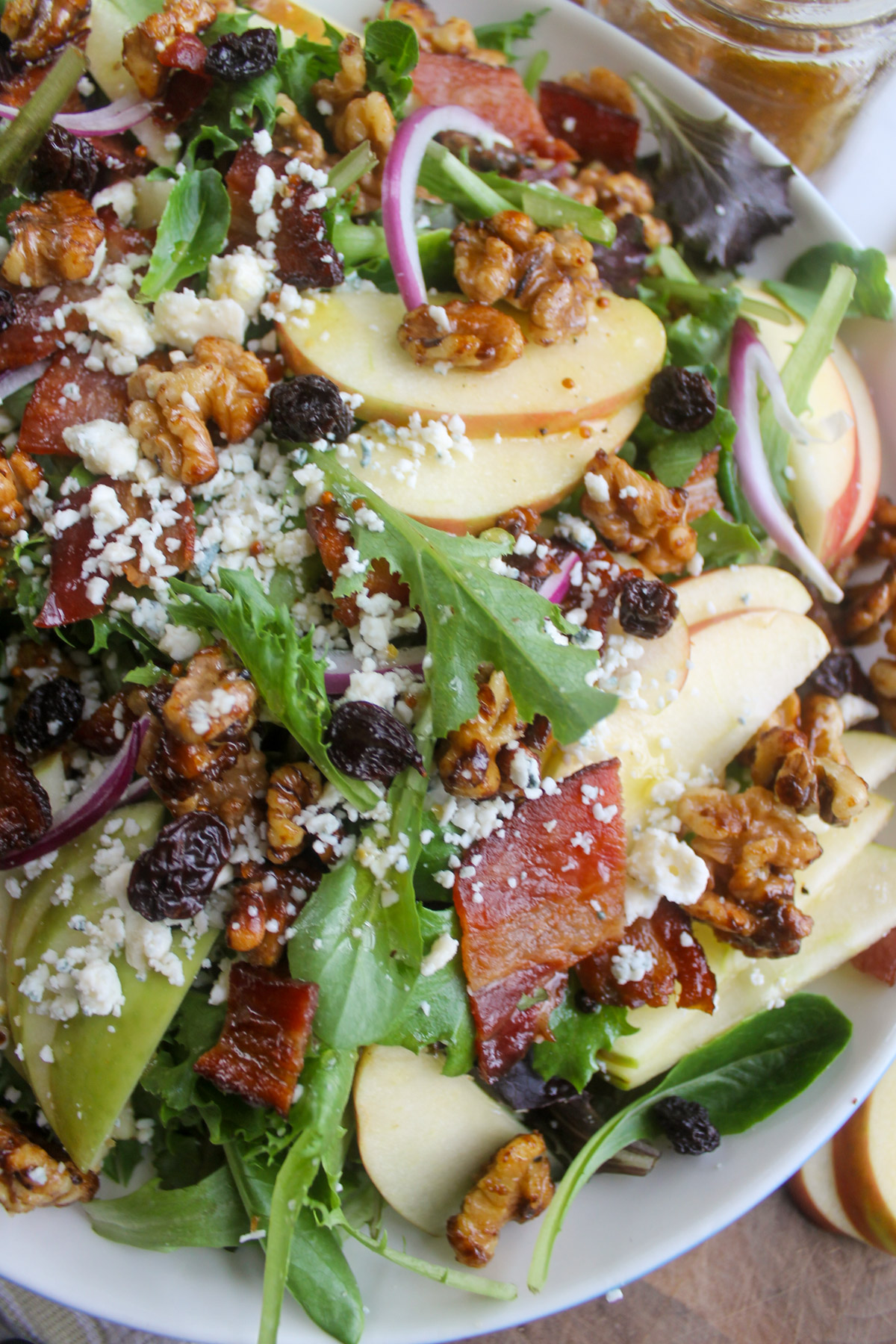 An apple salad on a platter with bacon, raisins, walnuts and blue cheese.