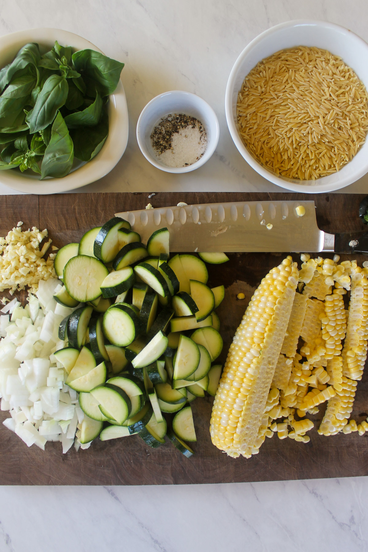 Chopped zucchini, onion, garlic, and corn cut off the cob on a cutting board.