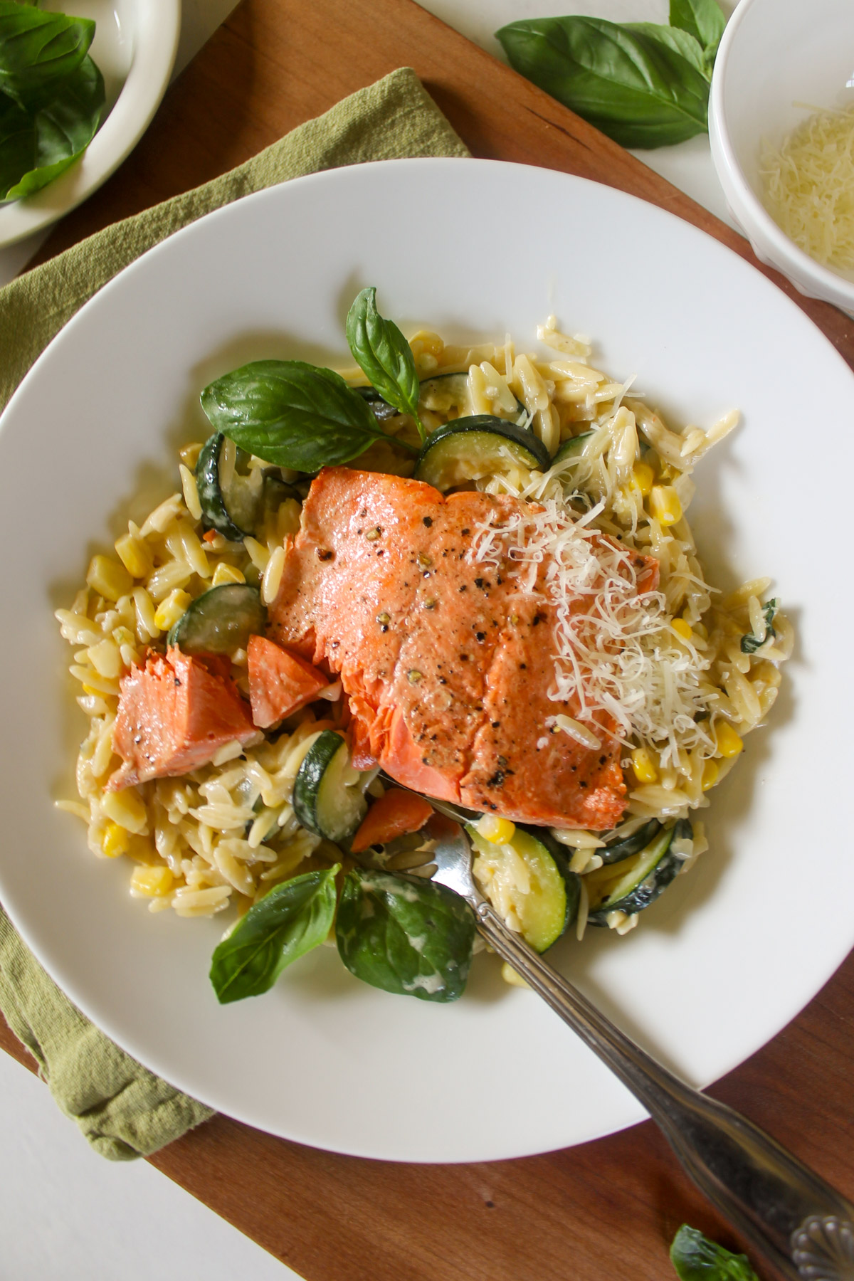 A plate of salmon on top of creamy orzo with corn, zucchini and basil leaves.