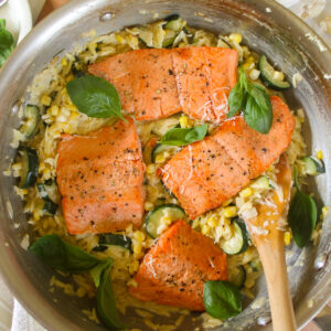 A skillet of zucchini orzo pasta topped with salmon and basil.