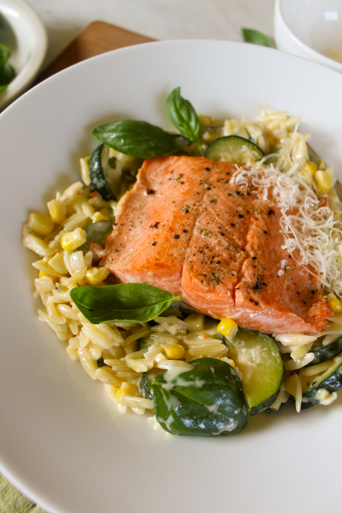 A white plate of salmon zucchini pasta with basil leaves.