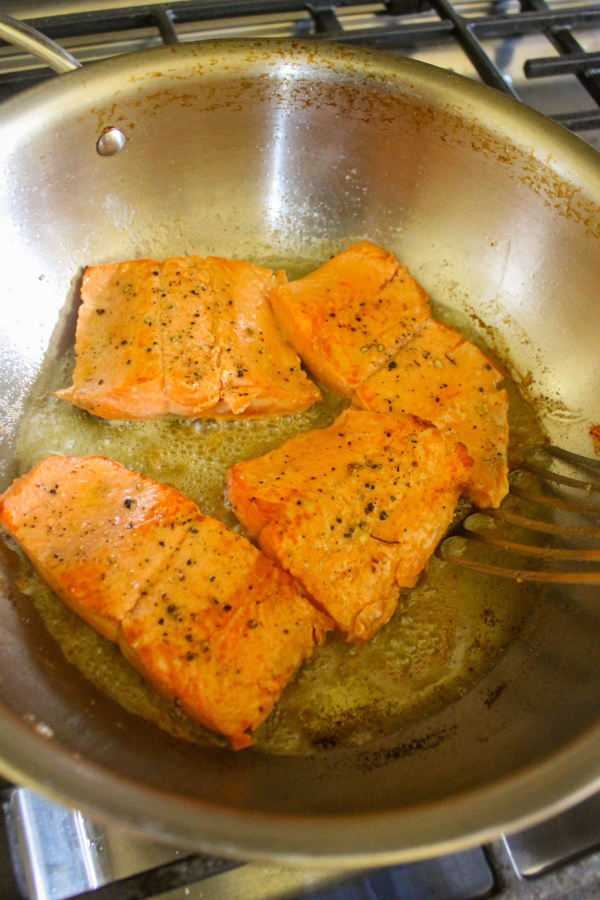 Pan frying four salmon filets in a skillet.