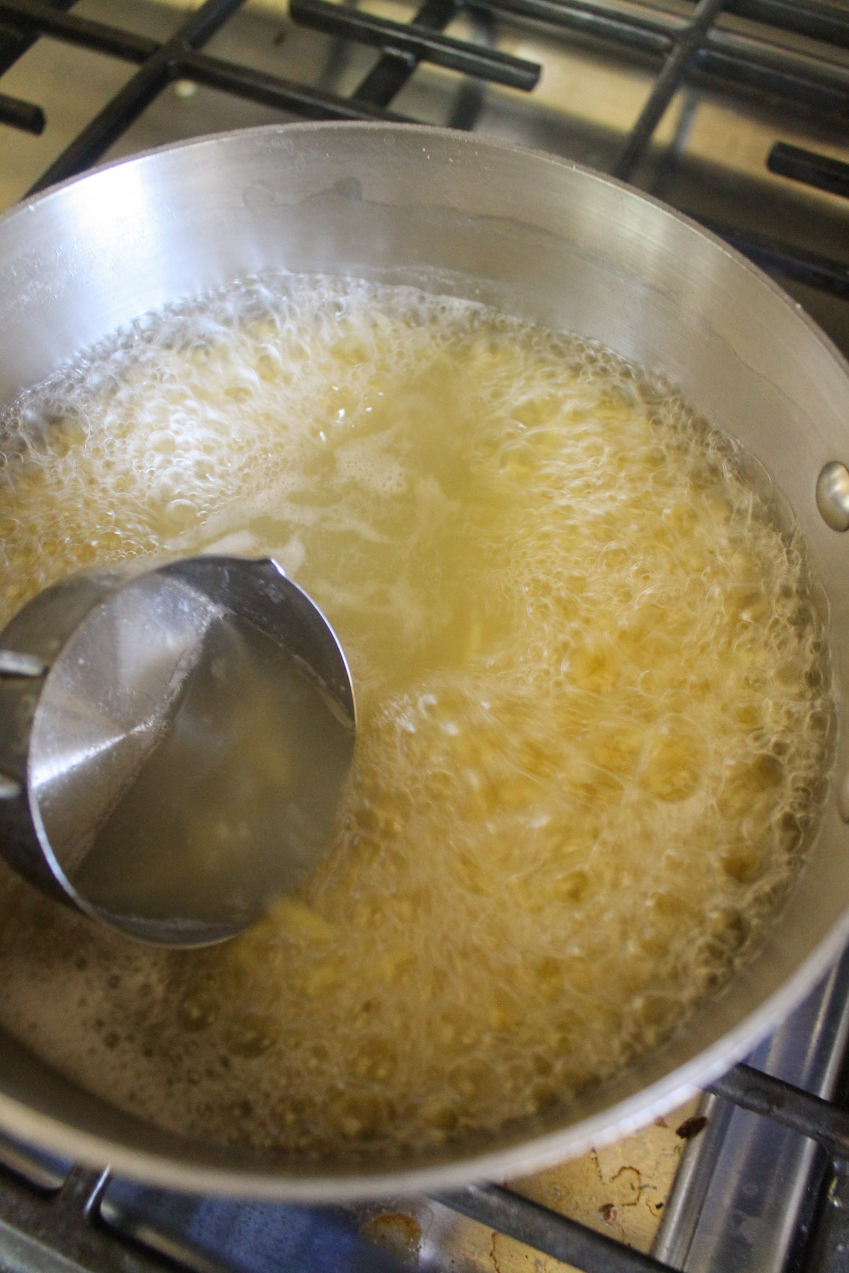 Dipping a measuring cup into boiling pasta water to save the water for the sauce.