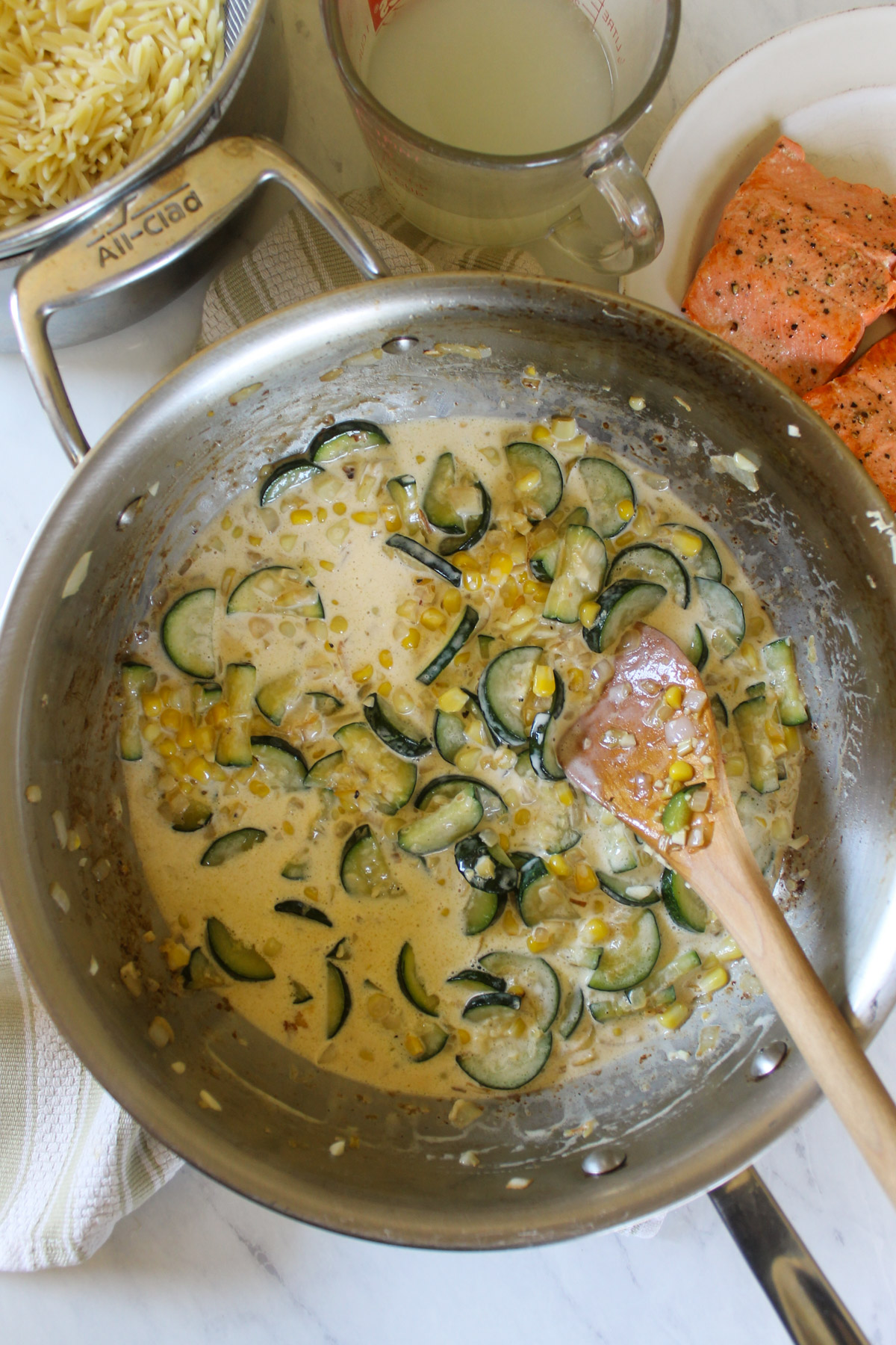 Cream added to zucchini and corn in a skillet to for a creamy white sauce.
