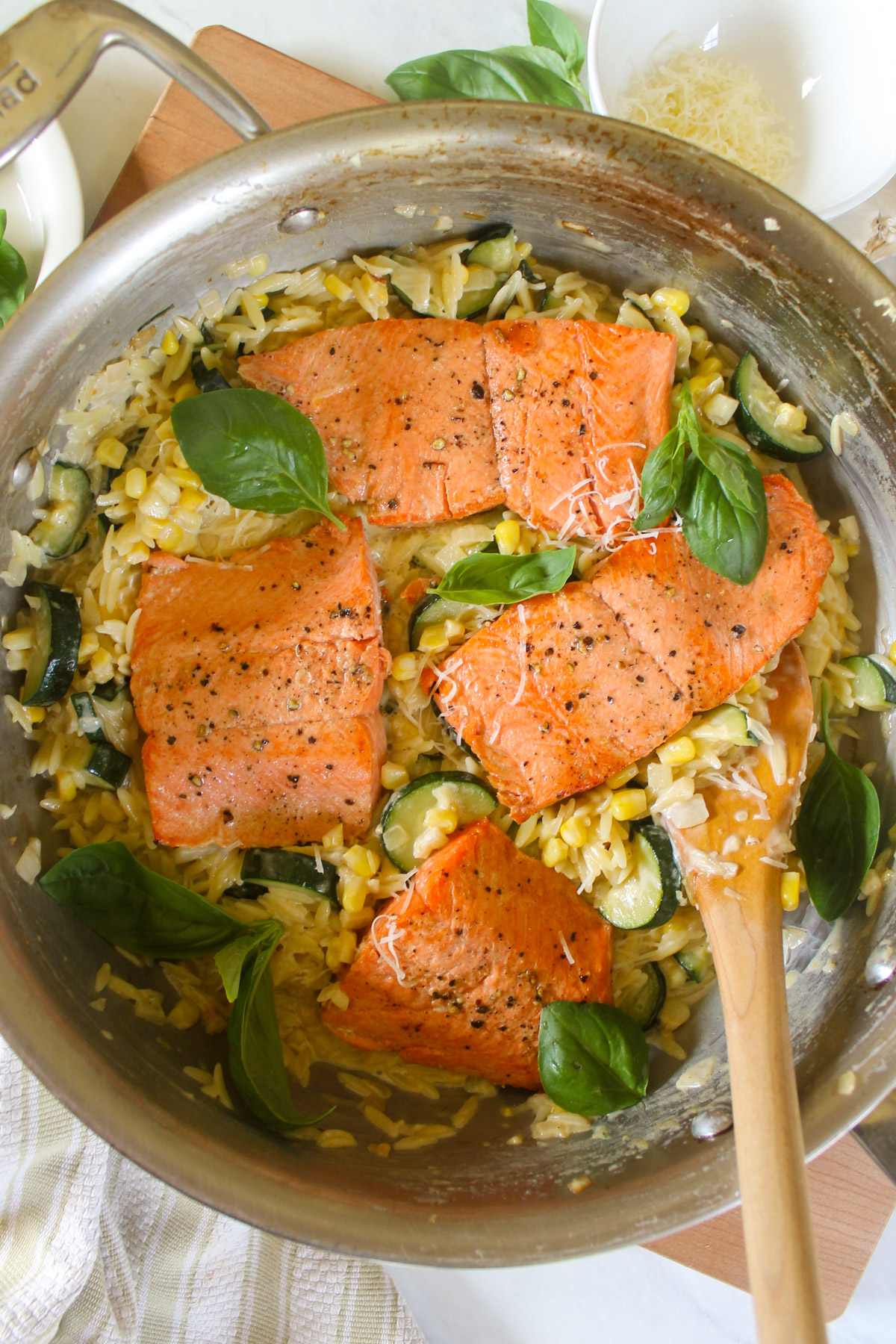 Salmon filets over orzo pasta with zucchini, corn and basil in a skillet.