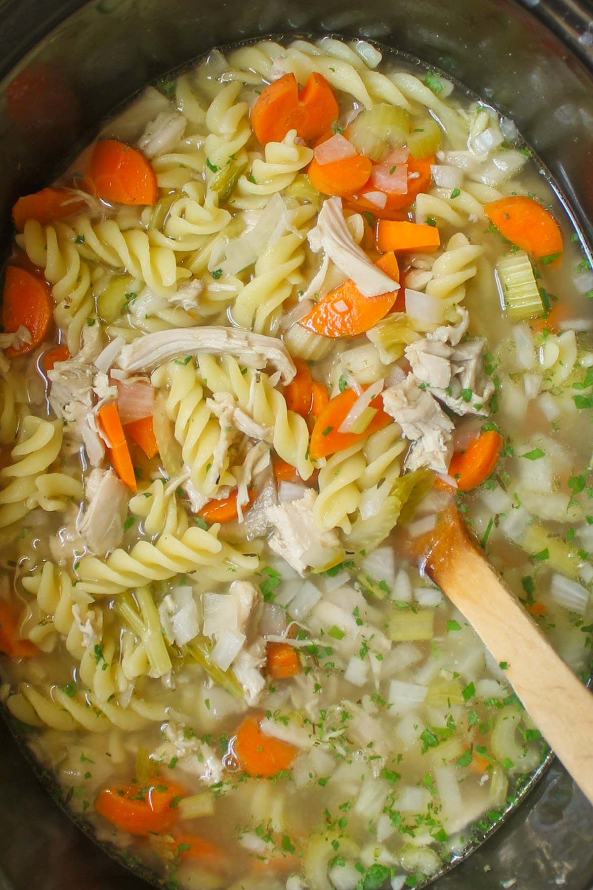 A crockpot full of chicken noodle soup with a wooden spoon.