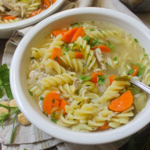Chicken Noodle Soup in a white bowl with herbs.