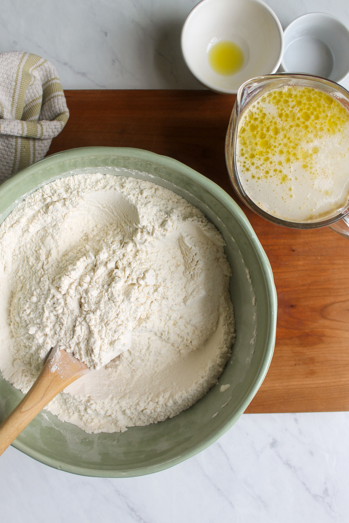 A green bowl of flour with a measuring cup of water, yeast and olive oil.