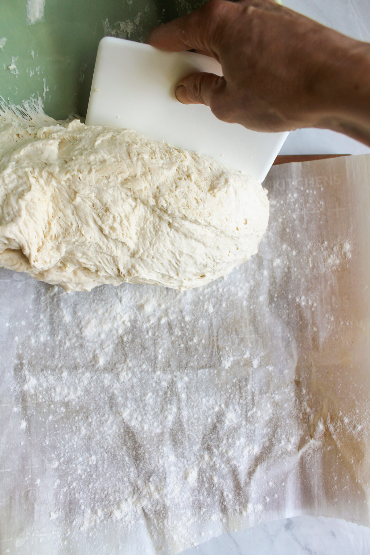 Removing the dough from the bowl onto floured parchment paper.
