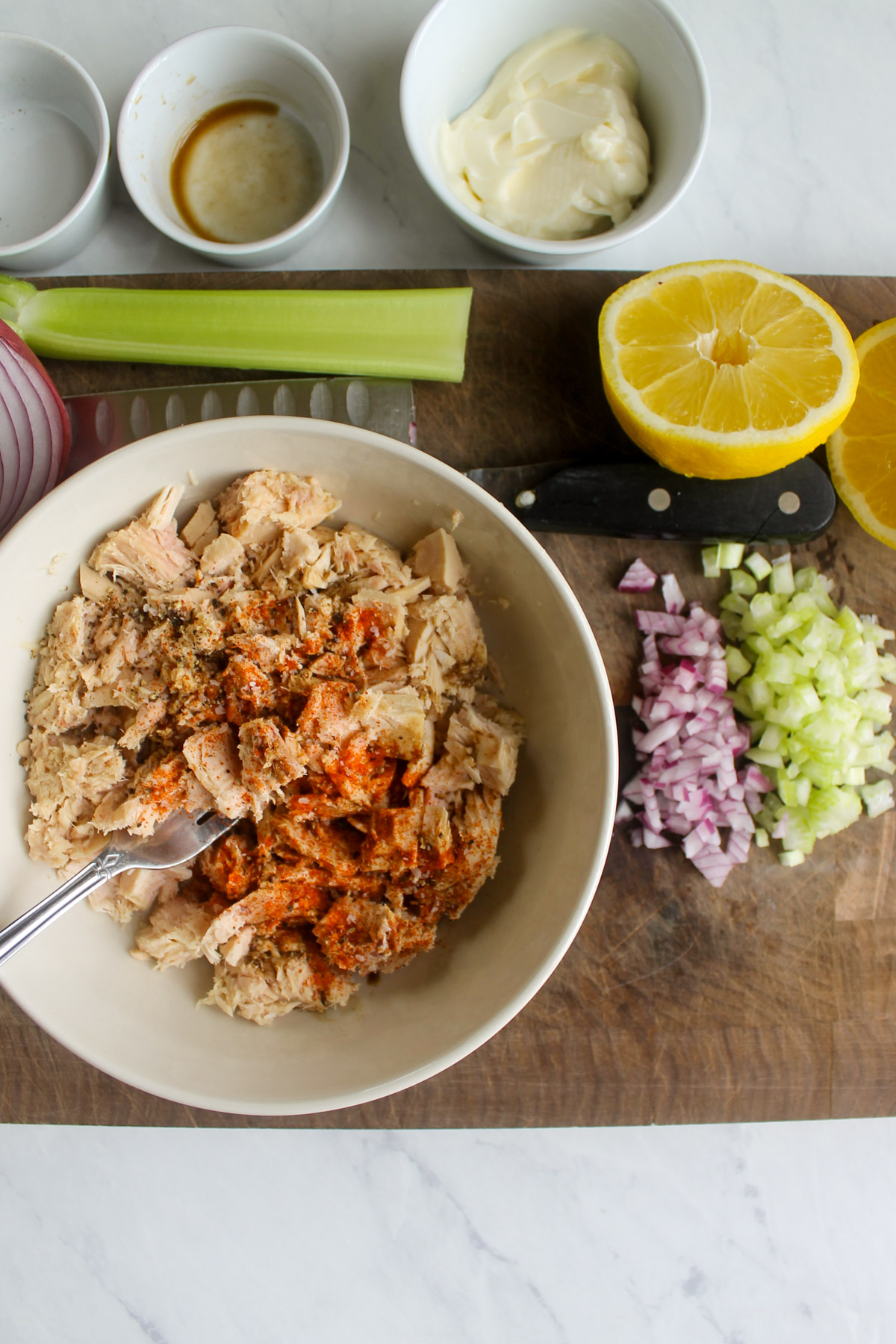 Tuna in a bowl with chopped celery and red onion on a cutting board.