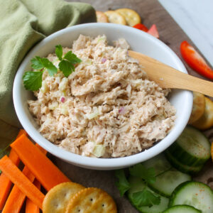 A bowl of tuna salad with veggies with crackers.