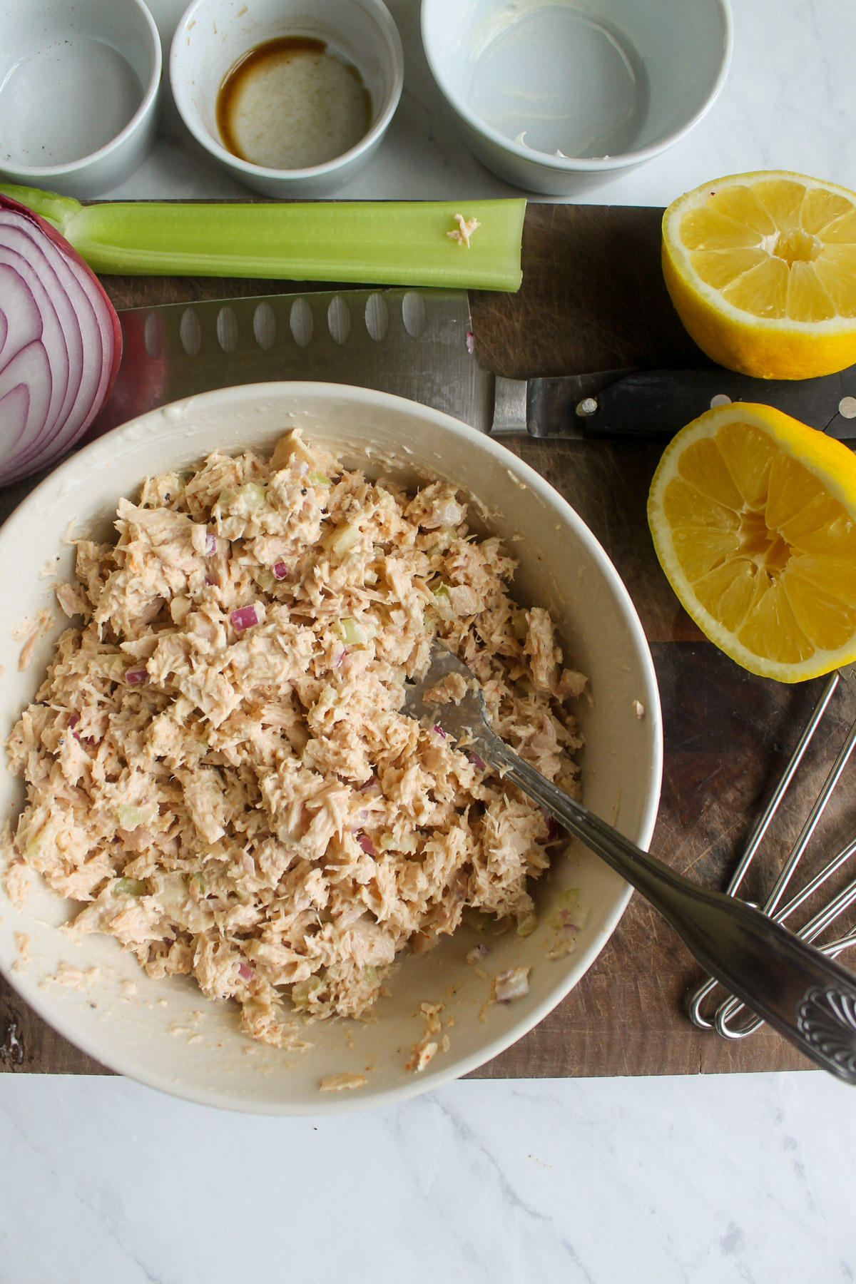 Mixed tuna salad in a bowl on a cutting board with a lemon.