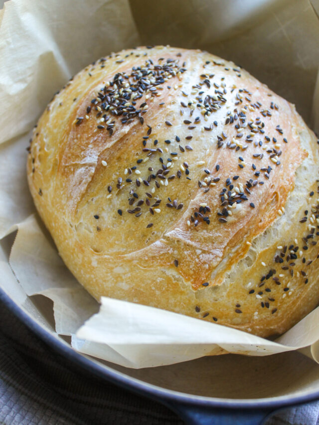 A loaf of seedy bread in a Dutch oven on parchment paper.