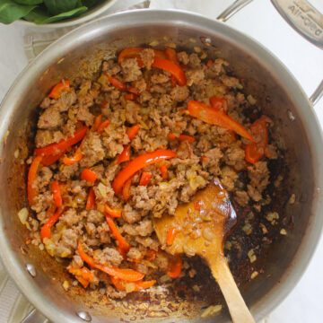Browned sausage in a skillet with onions and peppers.