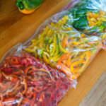 Three large ziploc bags of slice red, yellow and green bell peppers on the counter.
