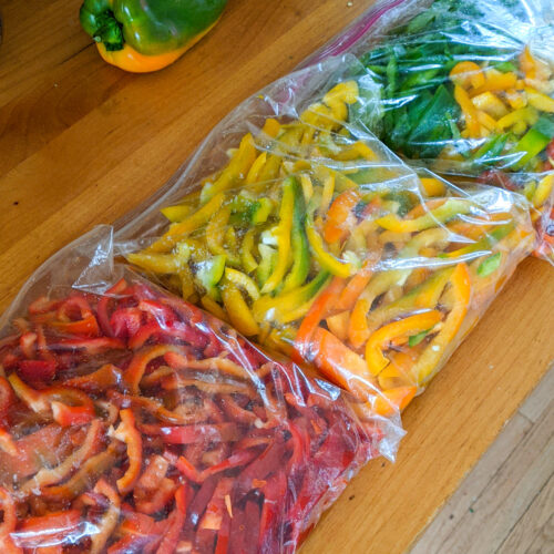 Three large ziploc bags of slice red, yellow and green bell peppers on the counter.