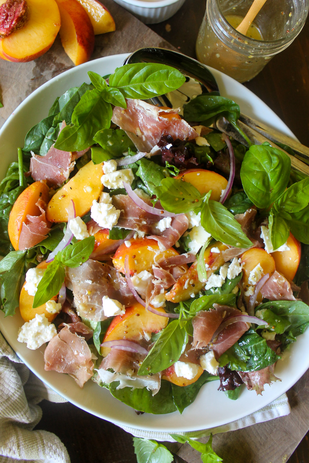 A platter of peach salad over lettuce with prosciutto and feta.