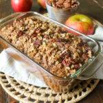 Apple pecan oat bread in a loaf pan with apples.