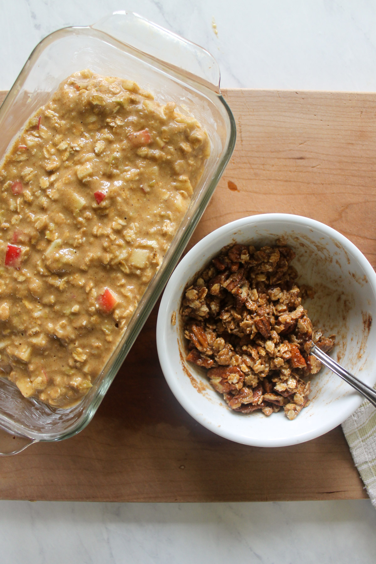 Apple bread batter in a loaf pan with a bowl of mixed oat topping.