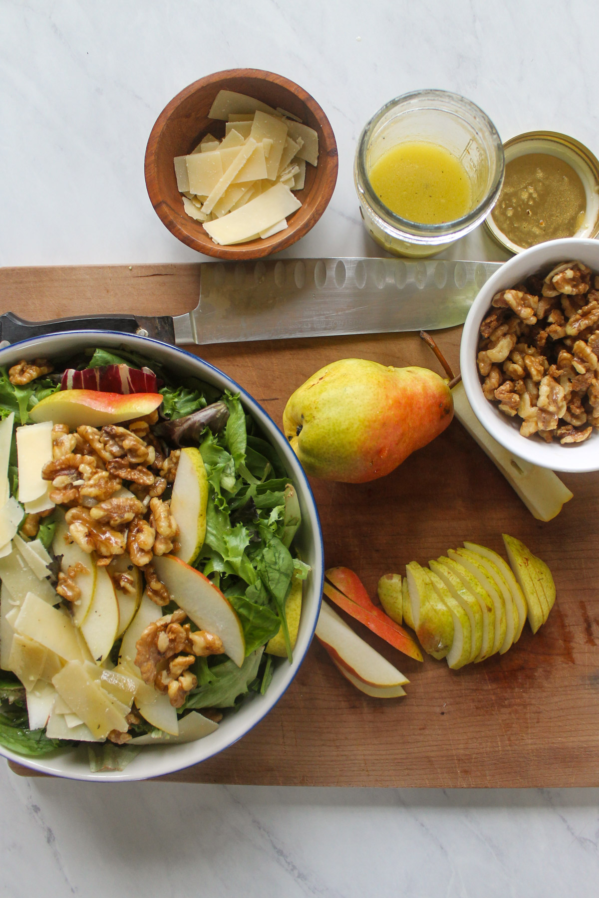 Pear slices and Parmesan cheese added to a mixing salad bowl with walnuts.