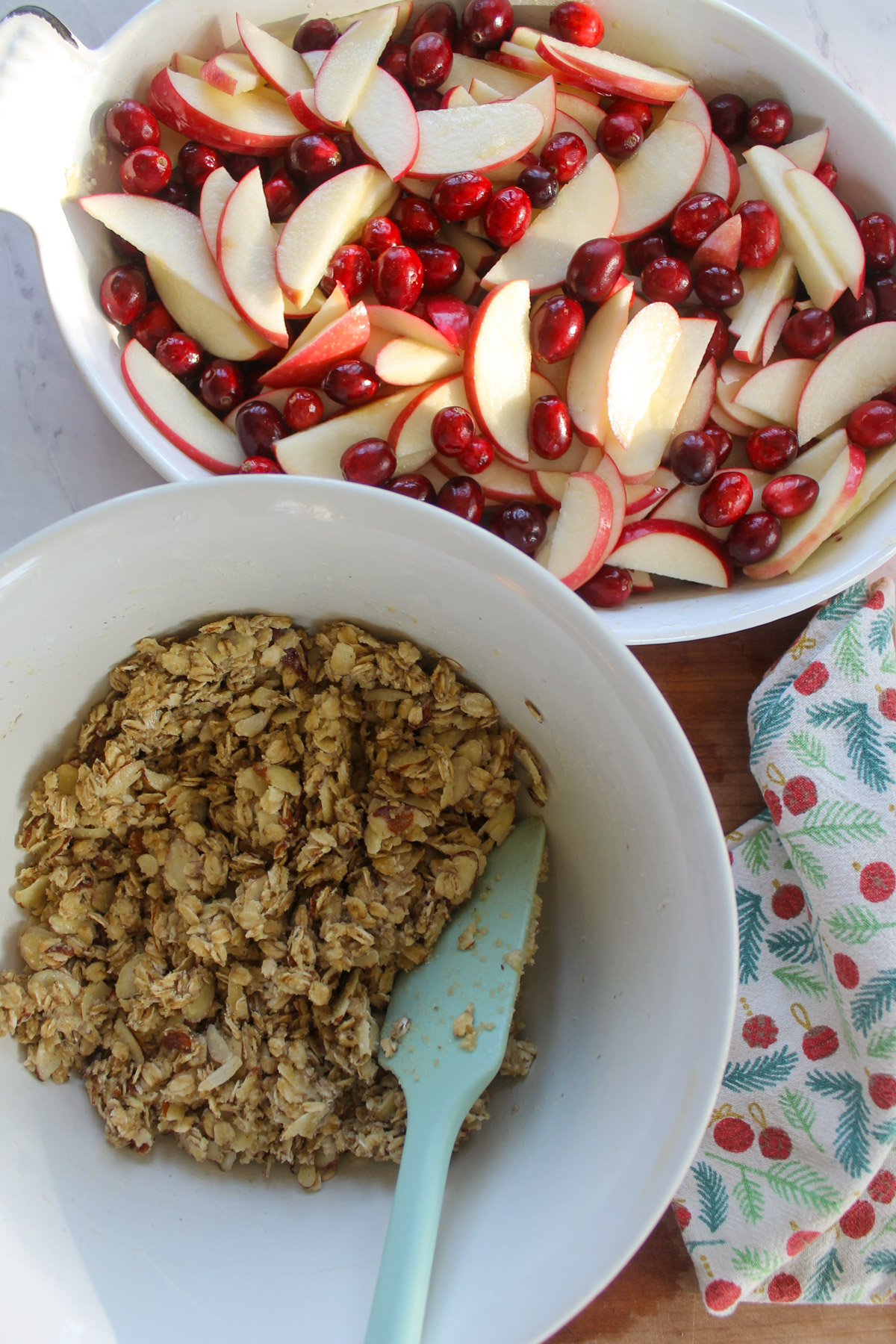 A bowl of oat almond topping next to a dish of apples slices and fresh cranberries.