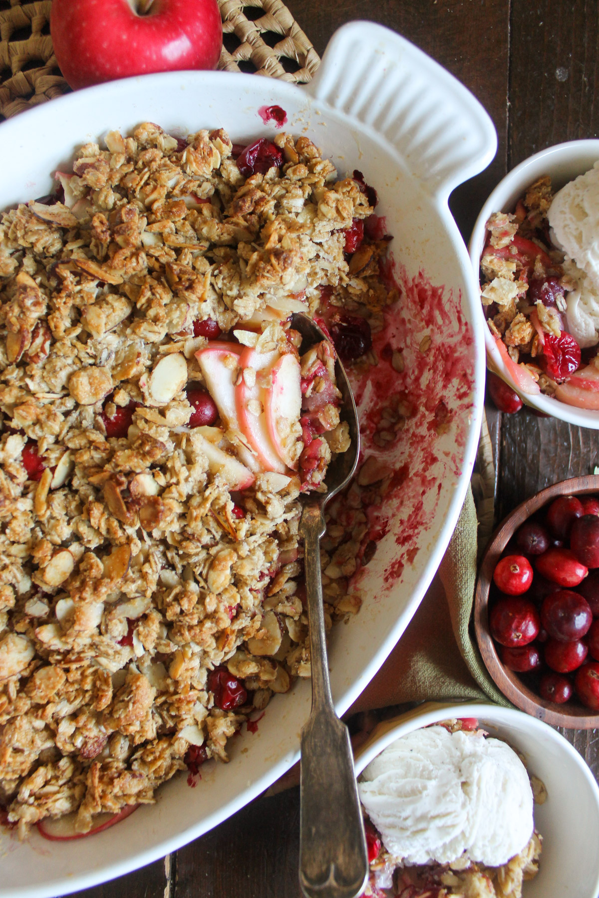 A baking dish of apple cranberry crisp with bowls with ice cream.