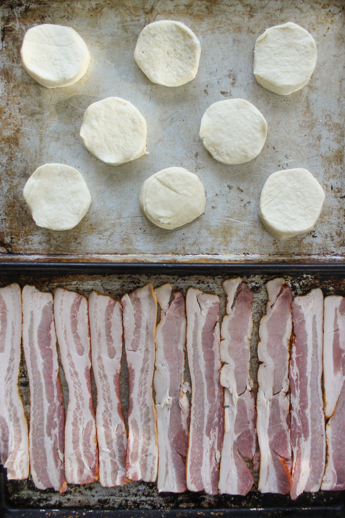 Raw biscuit dough and raw bacon on pans.
