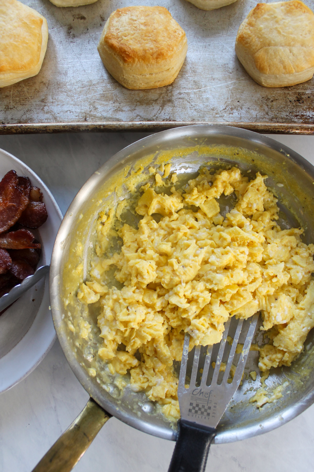 Scrambled eggs in a skillet with baked biscuits.