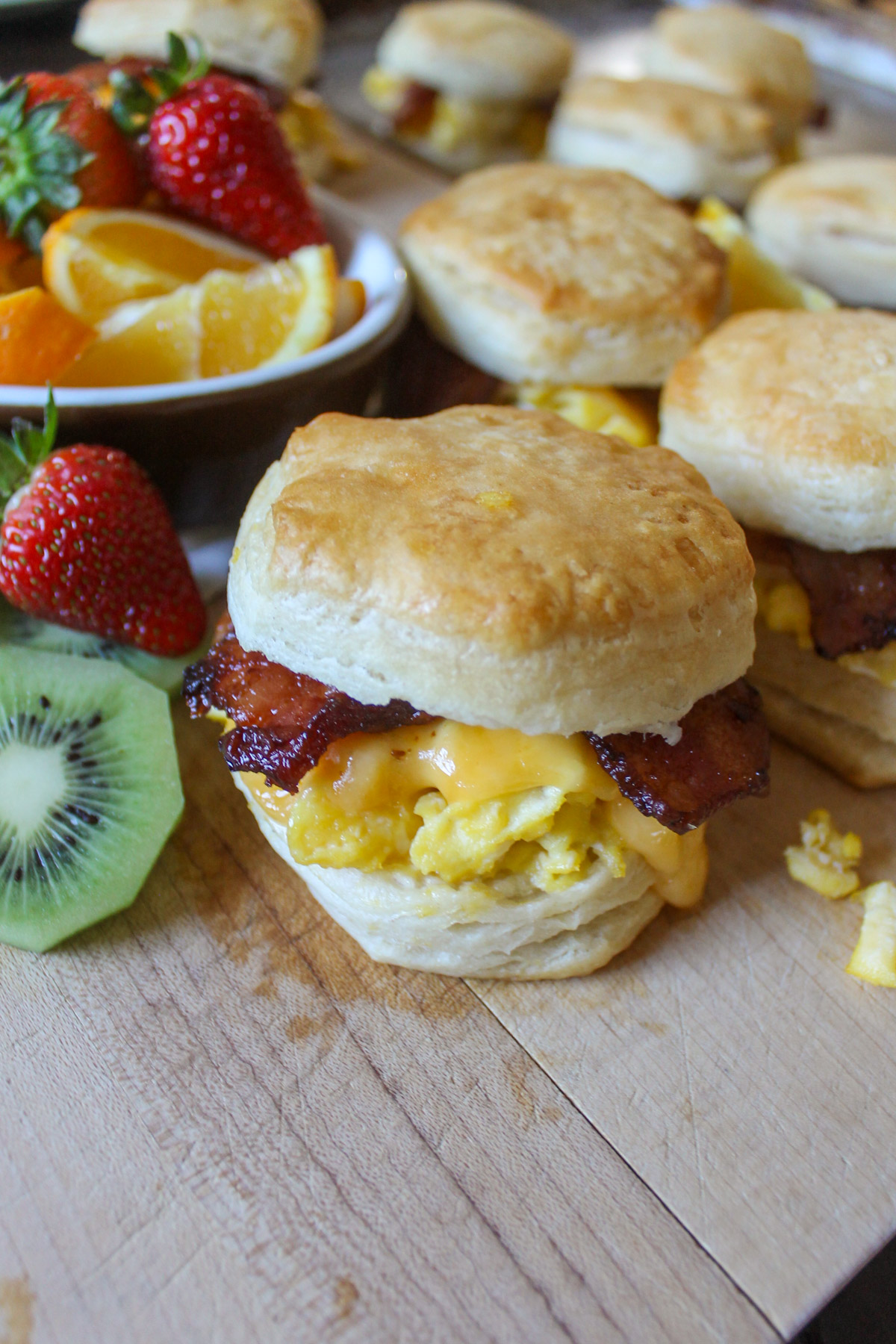 Biscuit breakfast sandwiches with bacon and cheese served with fruit.