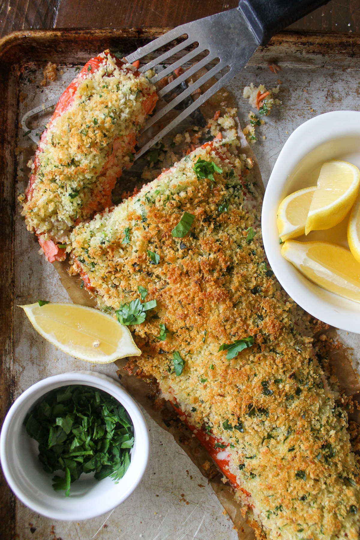 Oven baked panko crusted salmon on a sheet pan with lemon and fresh herbs.