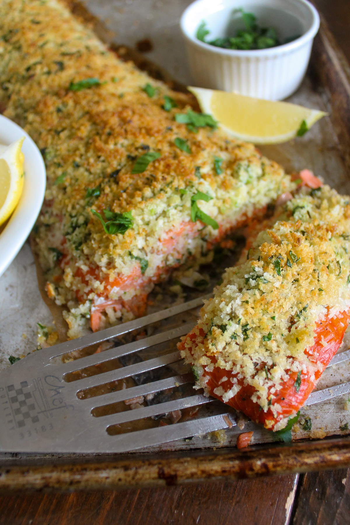 Baked panko crusted salmon filet on a sheet pan with a spatula serving.