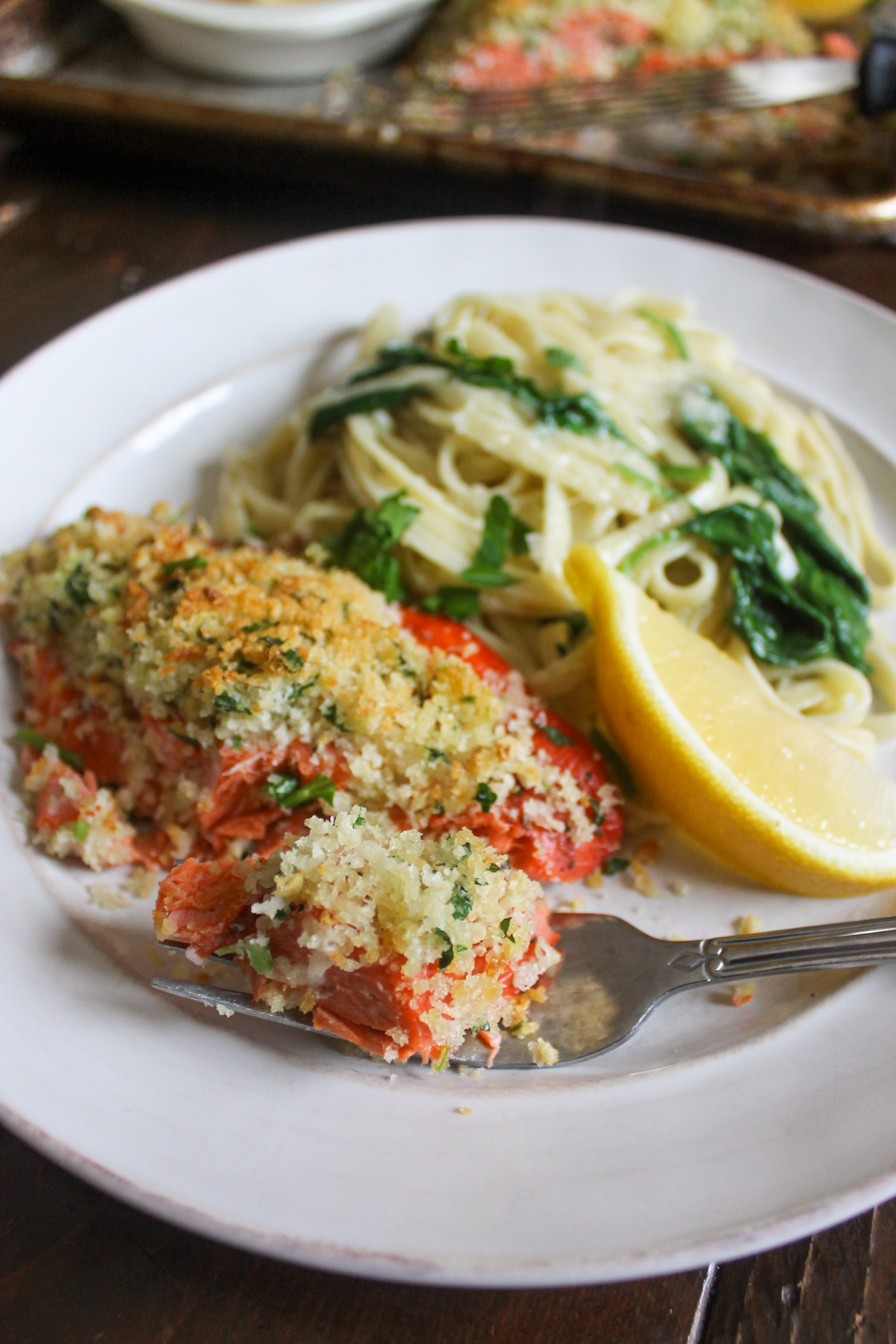 Panko crusted salmon on a plate with creamy spinach pasta and a lemon.