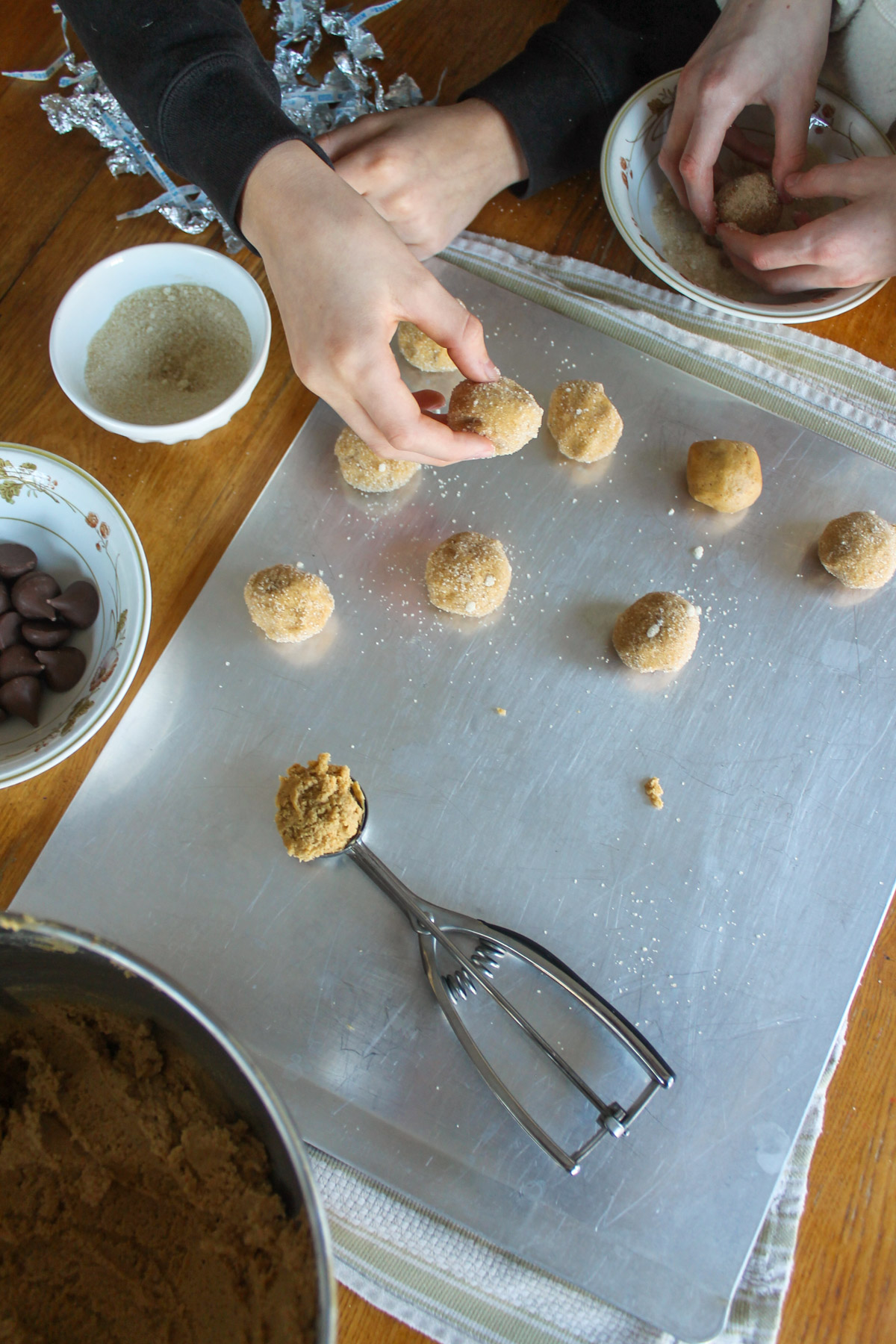 Rolling peanut butter blossoms into balls with sugar on a baking sheet.