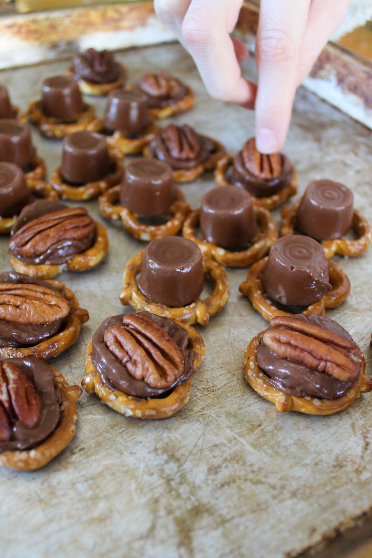 Pressing pecans into melted chocolate on pretzels.
