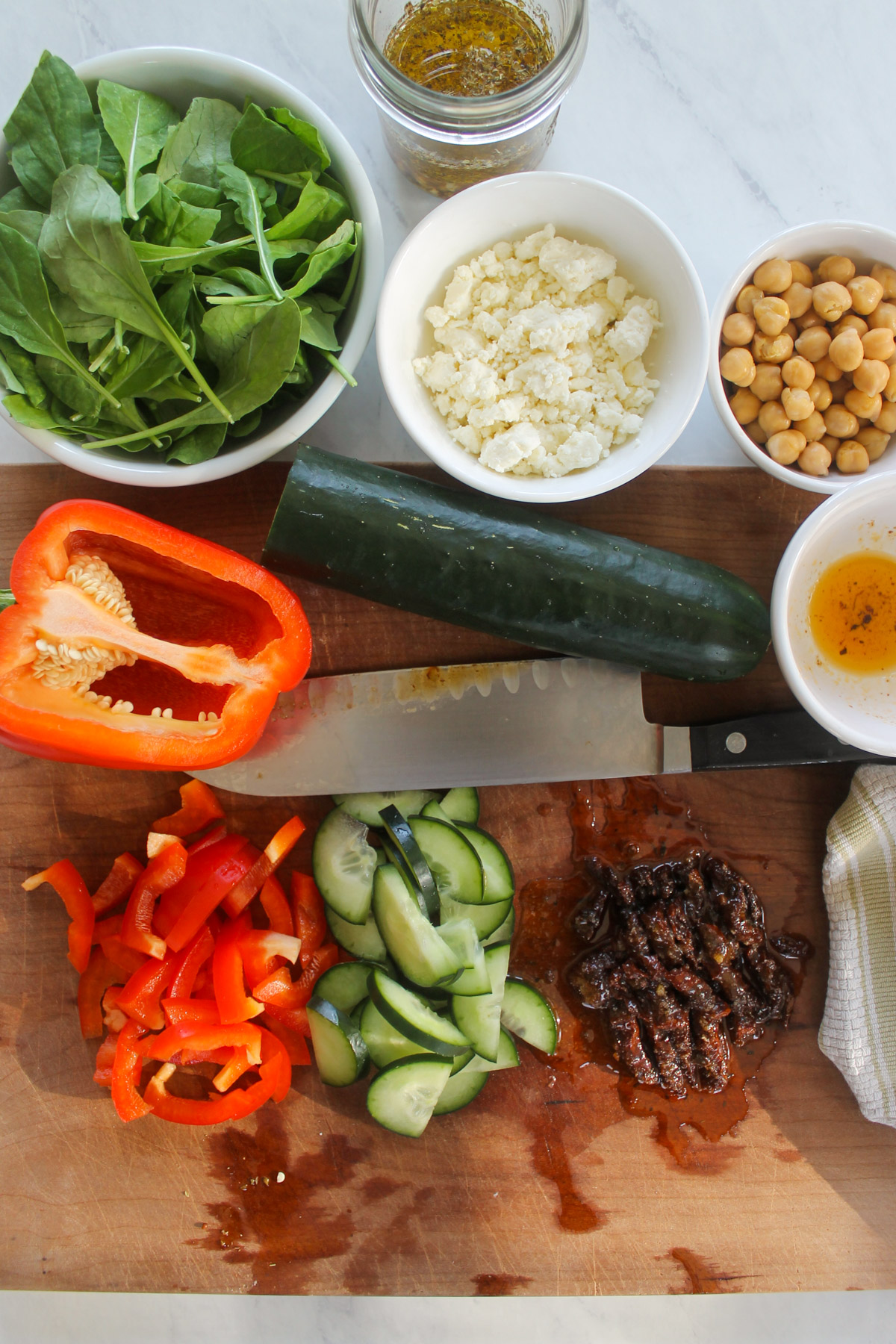 Bell Pepper, cucumber and sun-dried tomatoes sliced on a cutting board.
