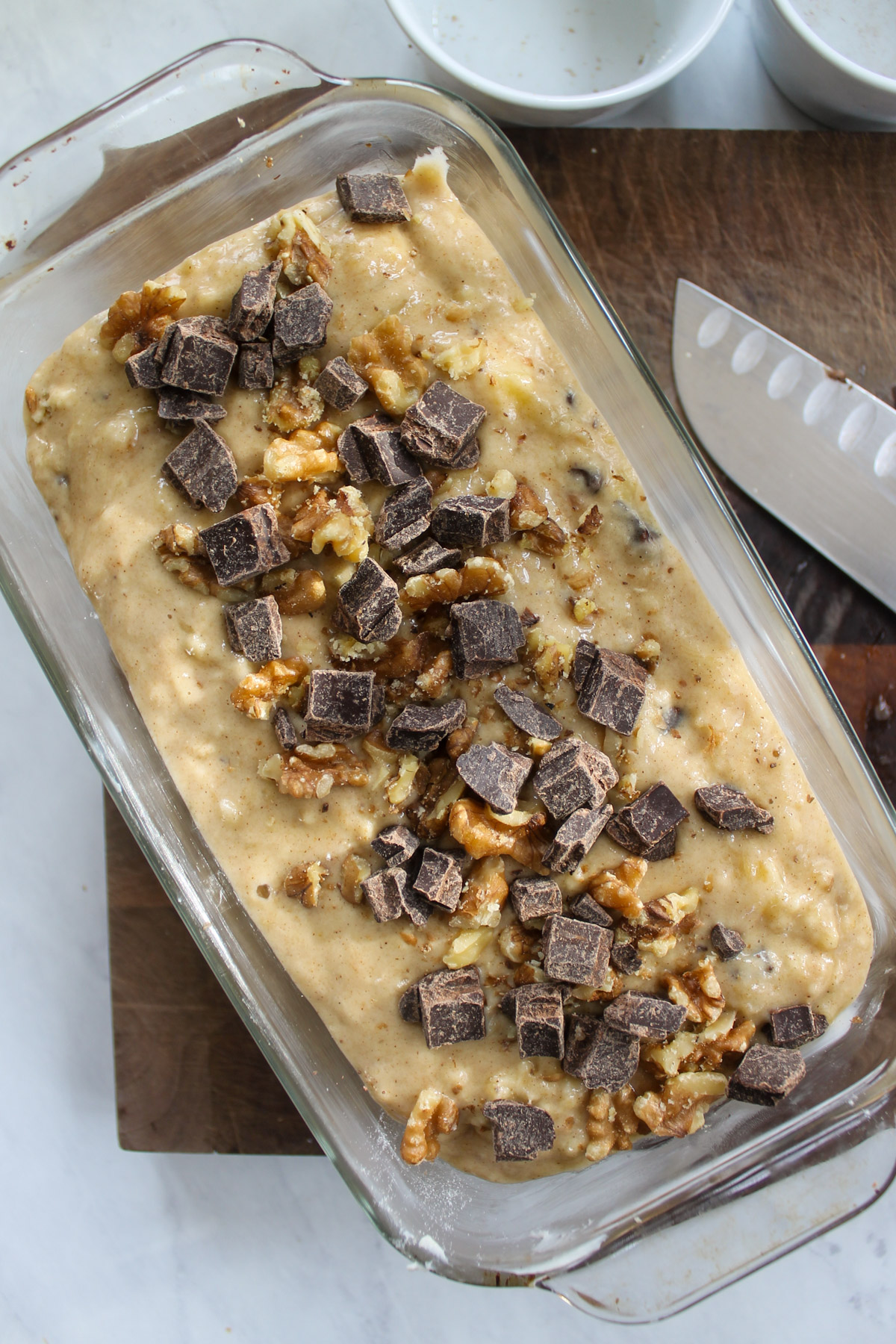 Unbaked banana bread batter in a loaf pan topped with chocolate and walnuts.